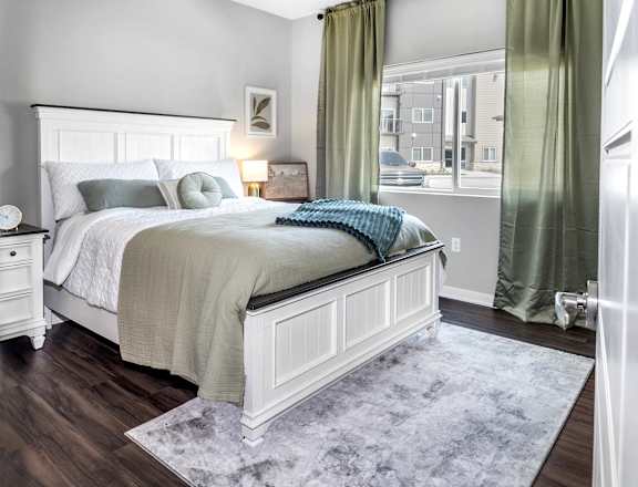 A bedroom with a large bed and a window with green curtains.