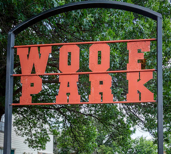 A black fence with a sign that says WOOF PARK.