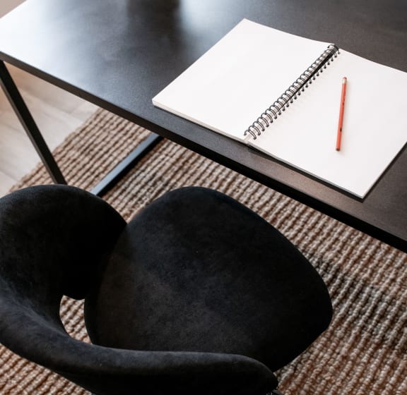 a black chair next to a table with a notebook and a desk