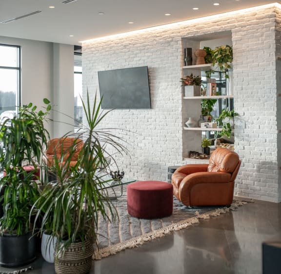 a living room with chairs and plants in front of a brick wall