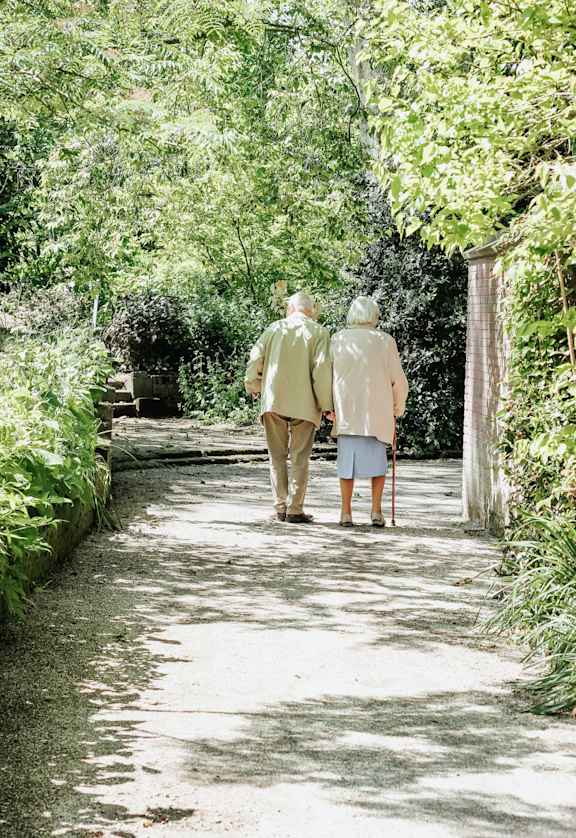 an elderly couple walking down a garden path