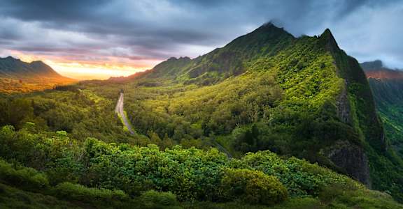 A mountain with a road leading to the top and a cloudy sky.
