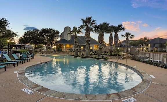 A large outdoor swimming pool surrounded by palm trees and lounge chairs.