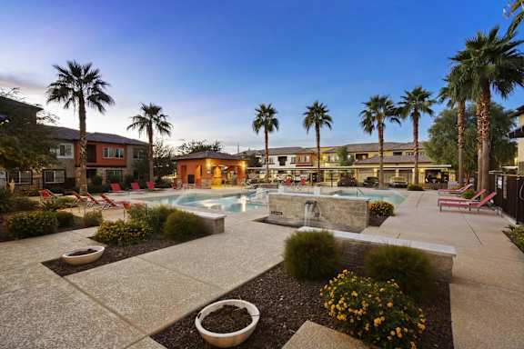 A pool surrounded by palm trees and a building in the background.