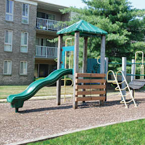 A playground with a green slide, wooden and metal swings, and a climbing frame. at The Apartments at Elmwood Terrace, Frederick, MD