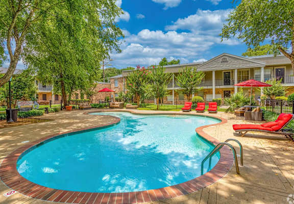 A swimming pool surrounded by a red brick border with a building in the background.