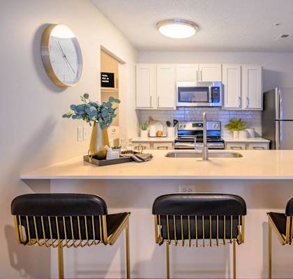 A kitchen with white countertops and black barstools.