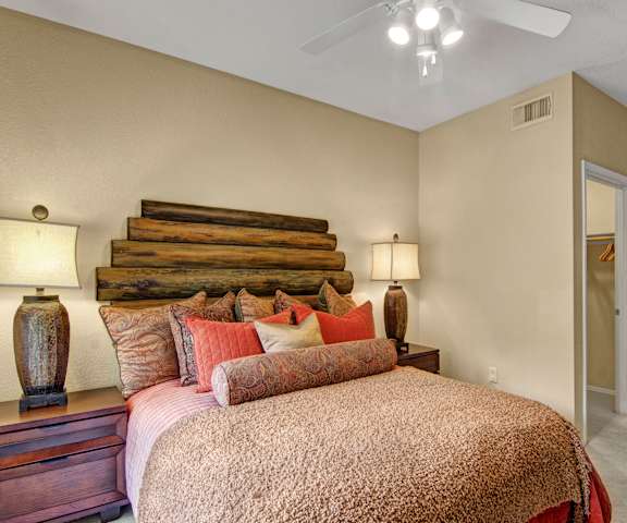 A spacious bedroom with a queen-size bed with a bedspread, a dresser, wall art, decorations, closet, and nightstands at Retreat at Speedway Apartment Homes. 