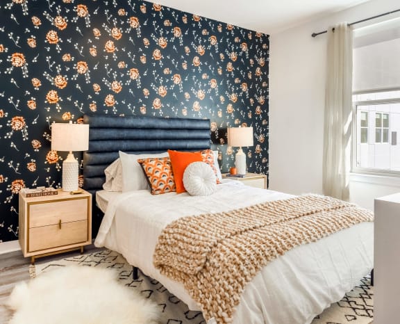 Model bedroom with blue wallpaper and a bed with orange pillows at Stella Apartments in New Carrollton, MD