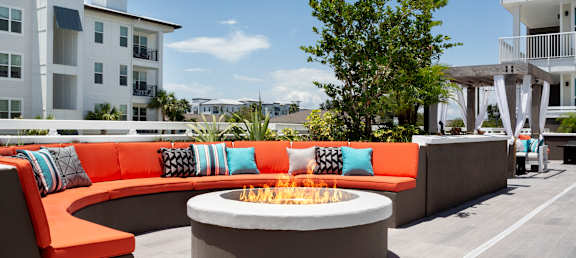 A modern outdoor seating area with a fire pit and orange couches.