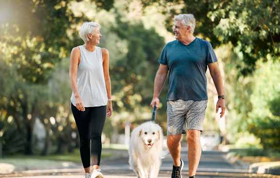 An older couple walking a dog in a park.