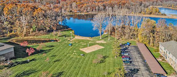 A beautiful aerial view of a park with a lake, trees, and a parking lot.