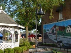 A white gazebo is surrounded by bushes and a street lamp.