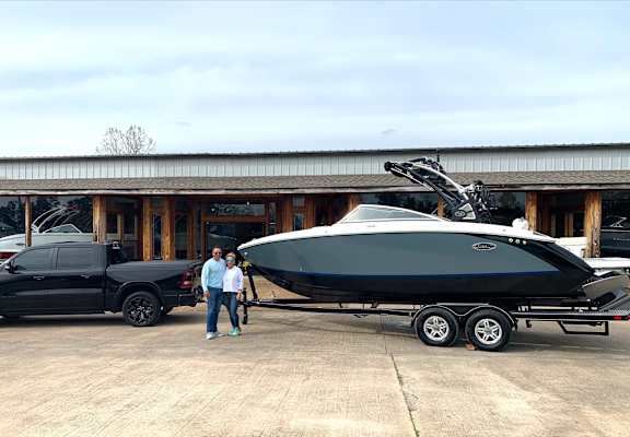 Two men stand next to a black boat and a black truck.