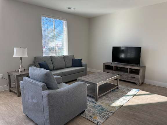 A living room with a grey couch, a grey armchair, a coffee table, and a television.