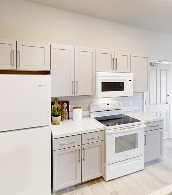 A white kitchen with a white fridge, white oven, white microwave, and white cabinets.