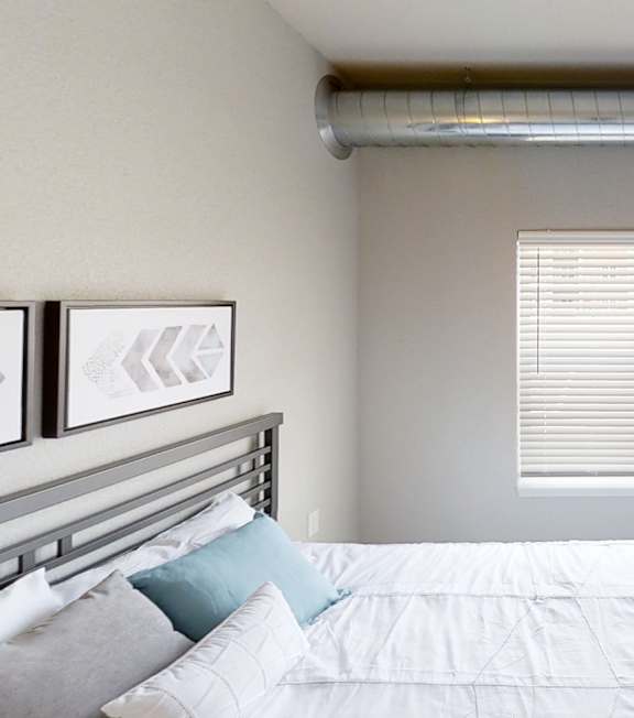 A bedroom with a bed, window with blinds, and a painting on the wall.