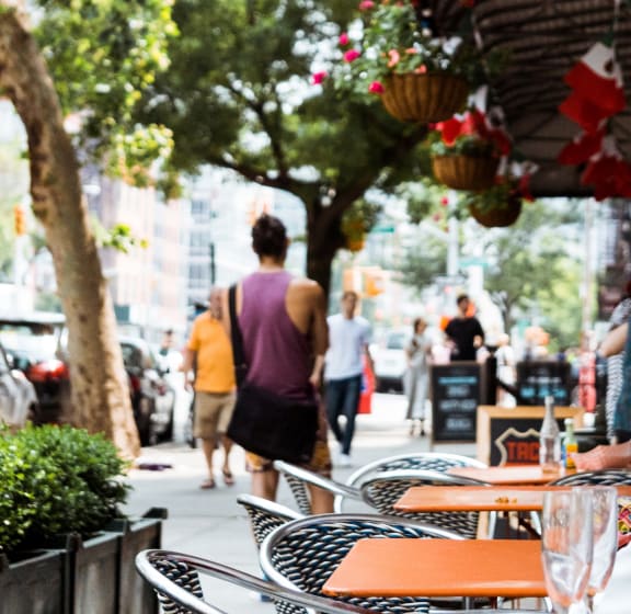 a man walking down a sidewalk with a table and chairs in the foreground