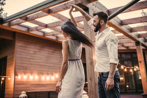A man and a woman are dancing together in a wooden-floored outdoor area.