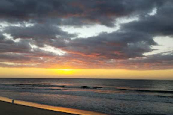 A beach at sunset with dark clouds in the sky.