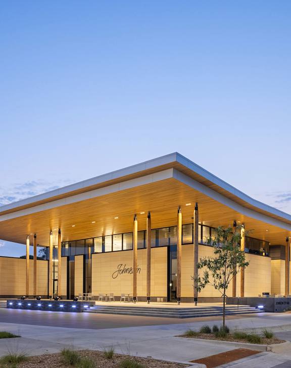 A modern building with a wooden exterior and a glass entrance is illuminated by lights.at Cornerstone Commons, Iowa, 50131