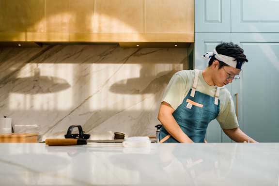 A man in a blue apron is leaning over a counter in a kitchen.