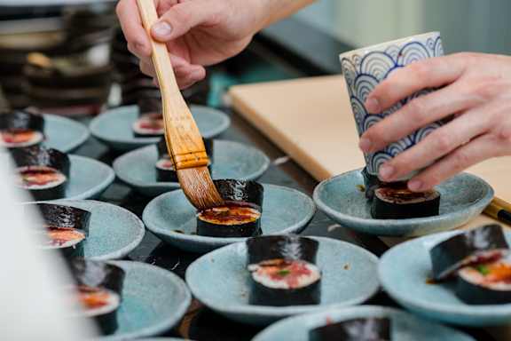 A person is preparing sushi with a wooden brush.