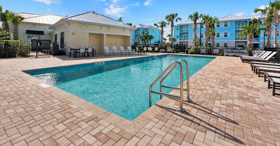 A swimming pool surrounded by a brick patio and lounge chairs.