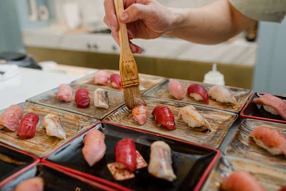 A person is preparing sushi with a wooden brush.