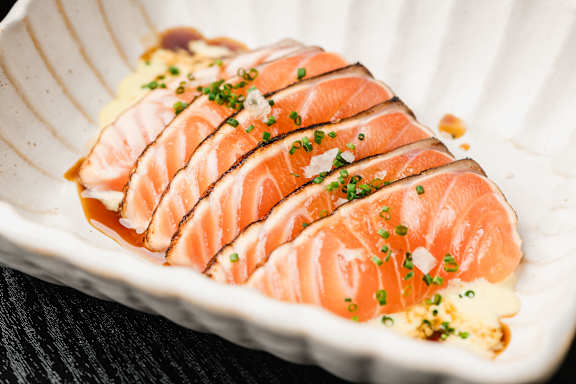 A plate of sliced salmon garnished with herbs and sauce.