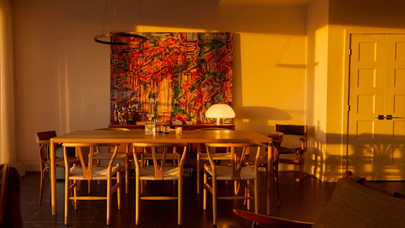 A dining room with a table and chairs and a large tapestry hanging on the wall.