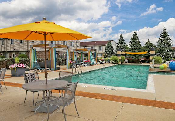 A yellow umbrella is on a patio table next to a pool.