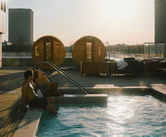 Two people sitting by a pool on a sunny day. at The Dale Apartments , Ontario, K1Y 4Y5