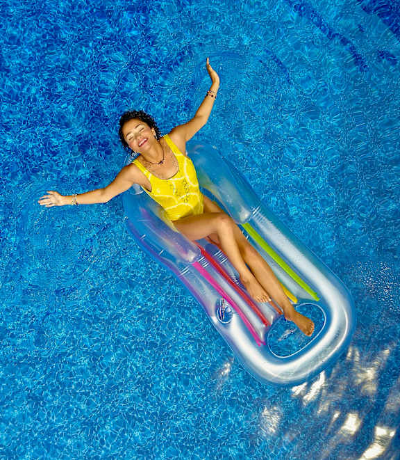A woman in a yellow dress is floating on a colorful inflatable in a pool.