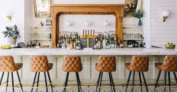 a bar with bar stools in front of a white counter with bottles of alcohol