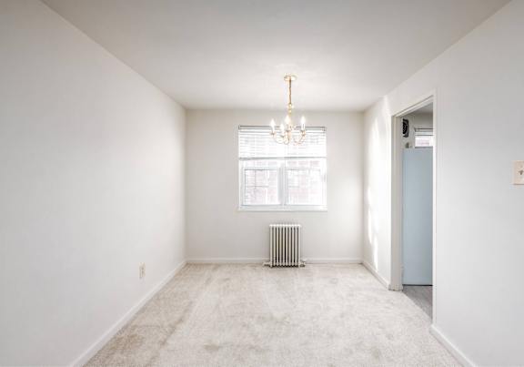 A room with a chandelier, a window with blinds, and a radiator on the floor.