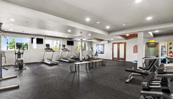 a gym with cardio machines and weights on the floor and a door