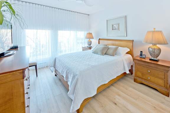 A bedroom with a bed, nightstand, and a plant.
