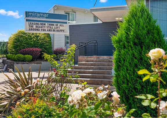A sign that says "Leasing now think of all the beauty still left around you and be happy" is displayed in front of a building.
