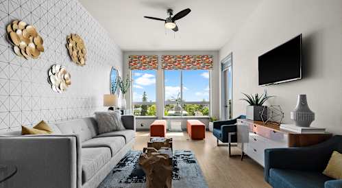 A living room with a grey sofa, orange ottoman, and a view of the city.