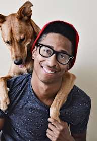 A man wearing glasses and a red beanie is holding a dog on his shoulder.at 2231 S Western, Los Angeles