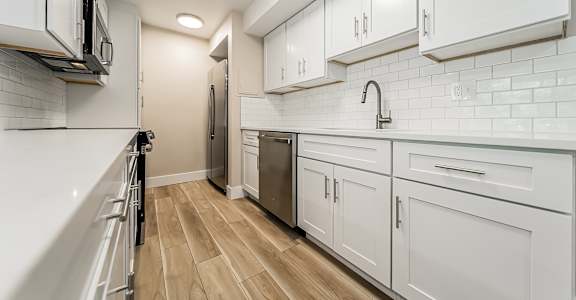 A kitchen with white cabinets and a wooden floor.
