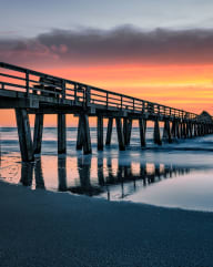 a fiery sunset paints the sky behind a pier on a beach
