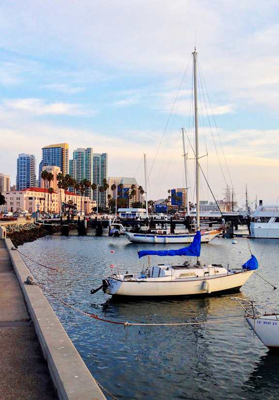 A boat with a blue sail is docked at a pier in a city.