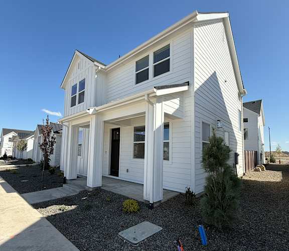 A white house with a gravel driveway and a small garden in front.at Alante Homes at Spring Run, Caldwell