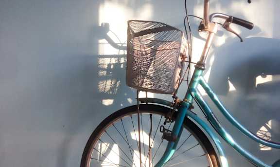 A blue bicycle with a basket is leaning against a wall.