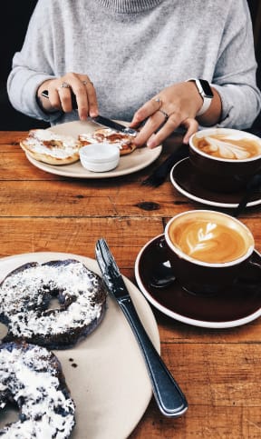 Woman Spreading Cream Cheese on Bagel in Front of Spread of Coffee and Bagels