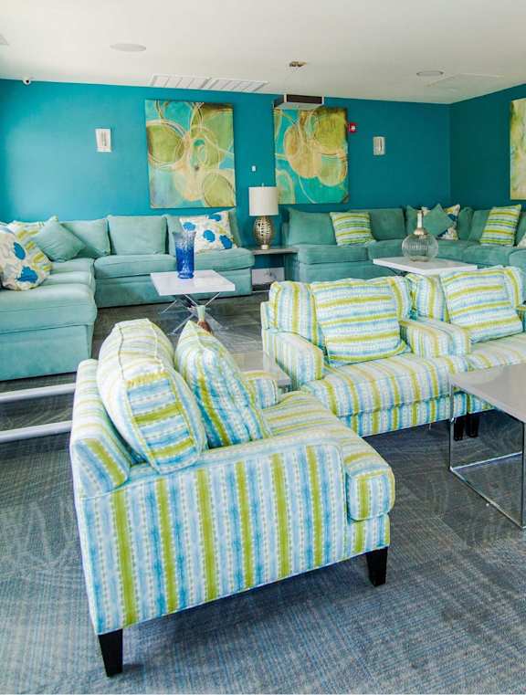 A living room with a blue couch and a painting of a beach scene on the wall.