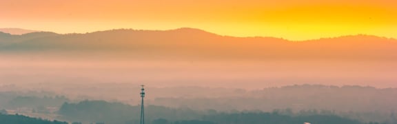 a view of the sunrise over mountains and a tower