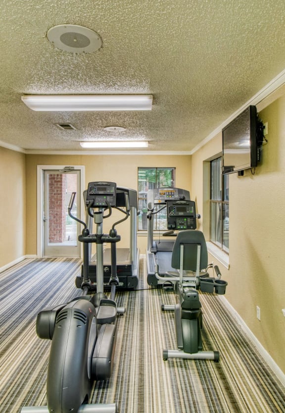two exercise machines in a gym with large windows at Village Oaks Apartments, Austin, Texas